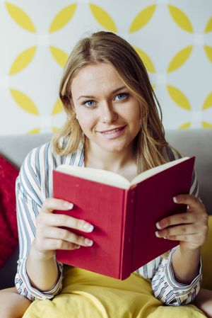 Young happy female reading book on sofa
