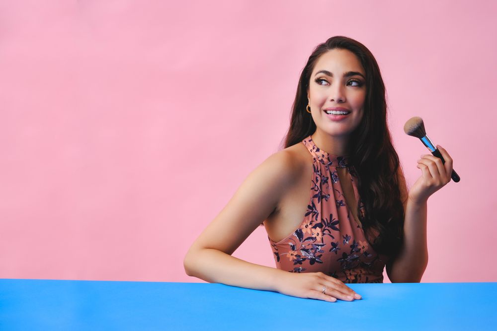 Elegant Hispanic woman with long brown hair holding large make up brush, copy space