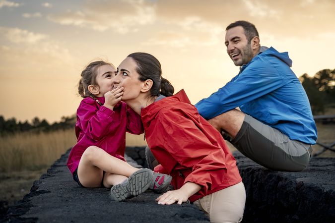 Daughter whispering a secret in her mother's ear during a family outing at sunset.