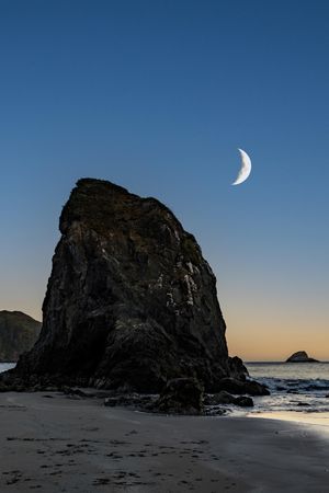 Crescent moon above quiet beach at dusk, vertical composition