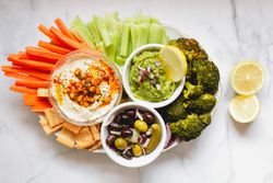 Tasty hummus and sauces decorated with bright cut vegetables on table