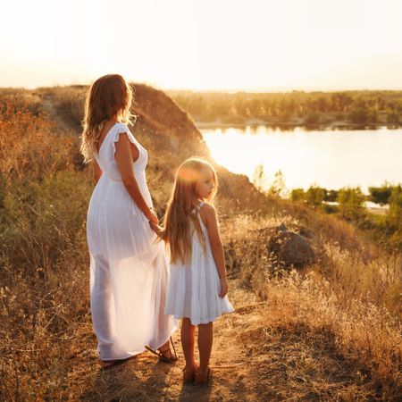 Woman and female child in summer dress enjoying the view of lake at dusk