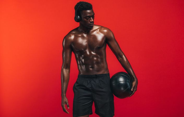 Shirtless man standing with medicine ball against red background
