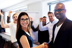 Happy male and female smiling and shaking hands in board room with colleagues celebrating