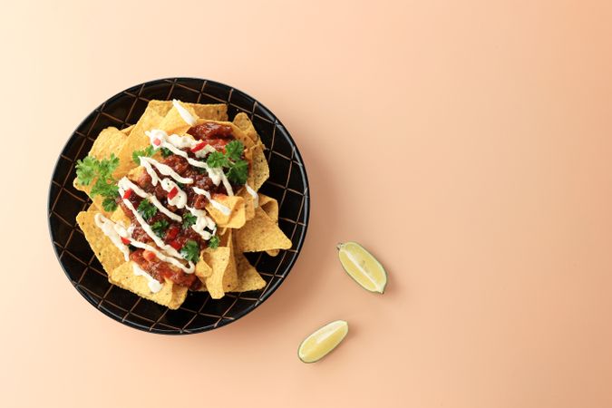 Top view of plate of nachos with salsa, sour cream, limes and cilantro