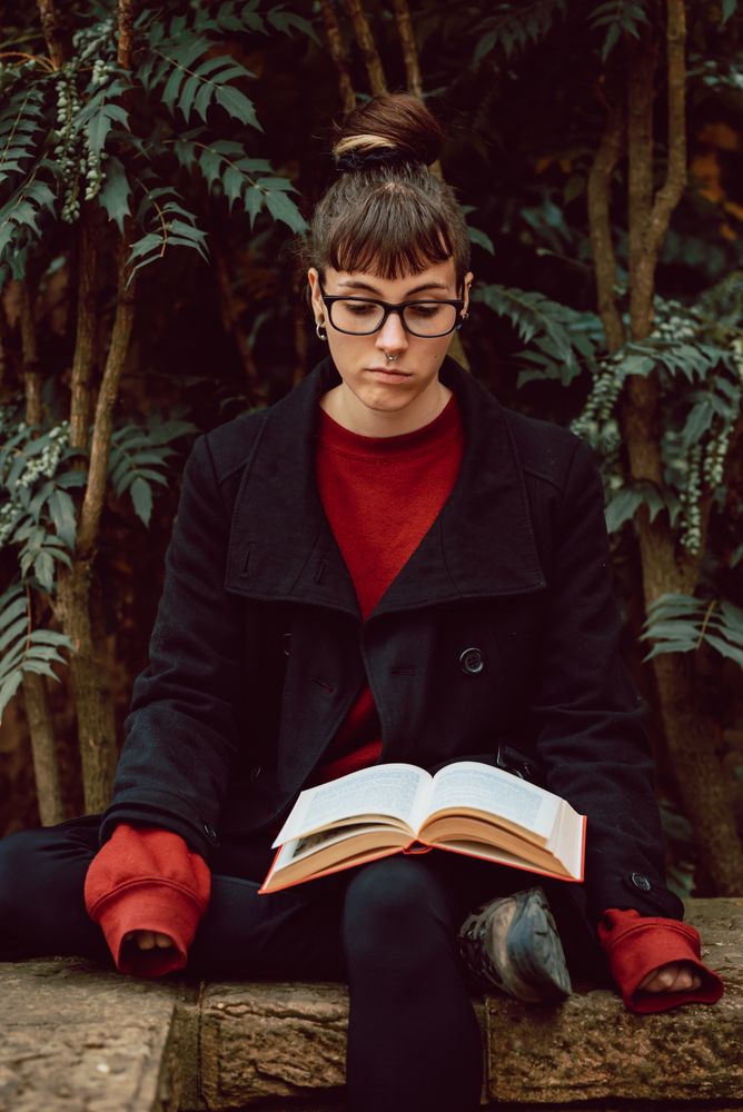 Young woman reading book on bench in park