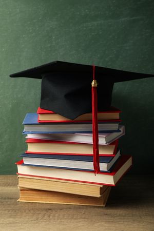 Graduation hat with books on a table on a dark background.