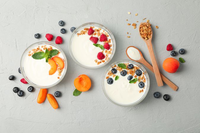 Flat lay composition with yogurt desserts and fruits on grey cement background
