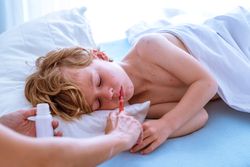 Crop mother giving medicine to sleeping son