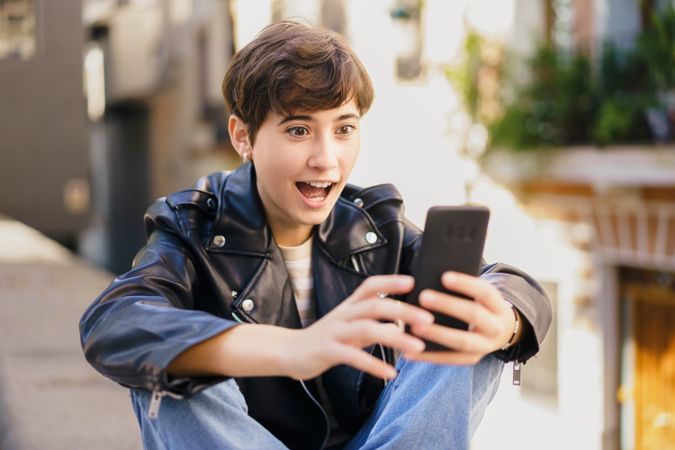 A cheerful young person is happily engaging with their smartphone in a bustling urban environment