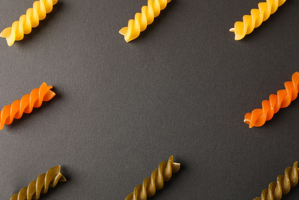 Flat lay composition with multicolored pasta on dark background, space for text and closeup