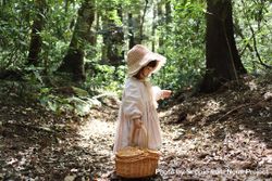 Girl wearing pink dress carrying brown woven basket standing in the woods 0LpNy0