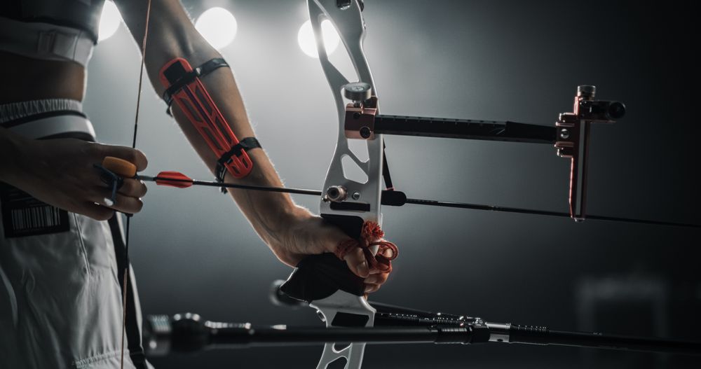 Low Angle Shot Of an Anonymous Female Archer Holding a Modern Compound Bow, Aiming at a Target. Young Athlete Drawing the Arrow in a Stadium Competition or a Dark Studio for Advertising