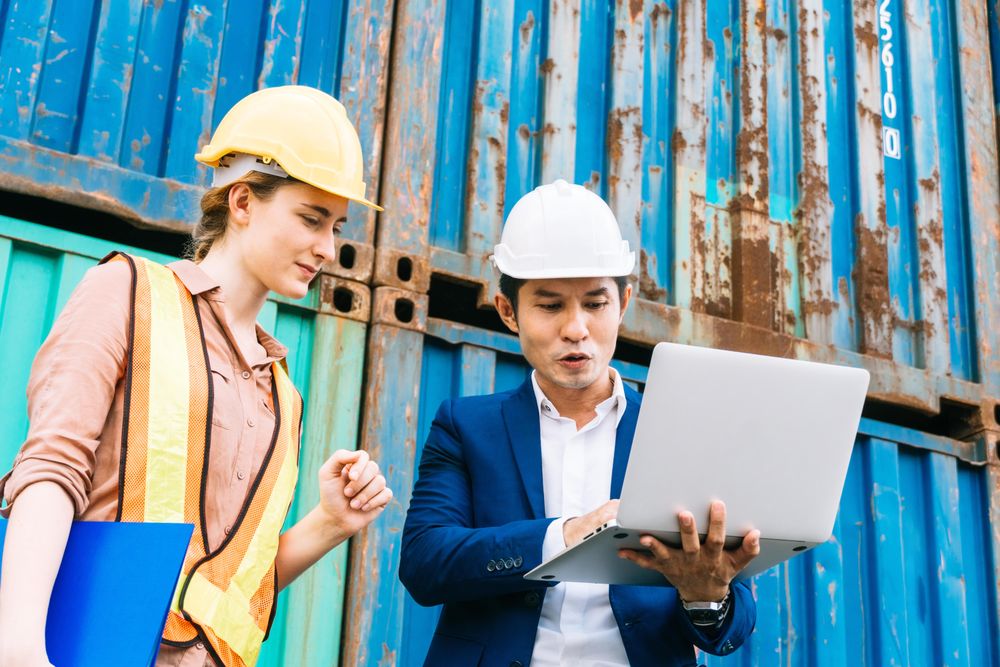 Male and female colleague onsite with hard hats and laptop