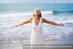 Older woman opening her arms on a tropical beach bYyA1b