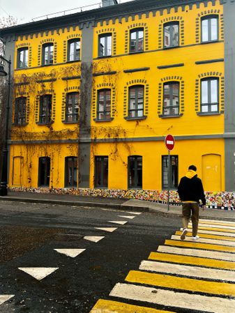 Back view of man in hoodie walking on pedestrian lane beside yellow building