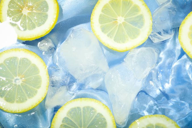 Top view of clear water with blue fabric, lemons and ice