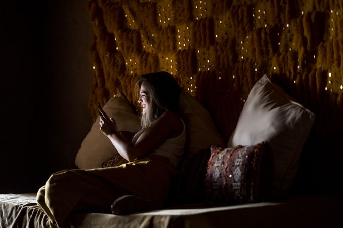 Smiling woman using smartphone in dark room