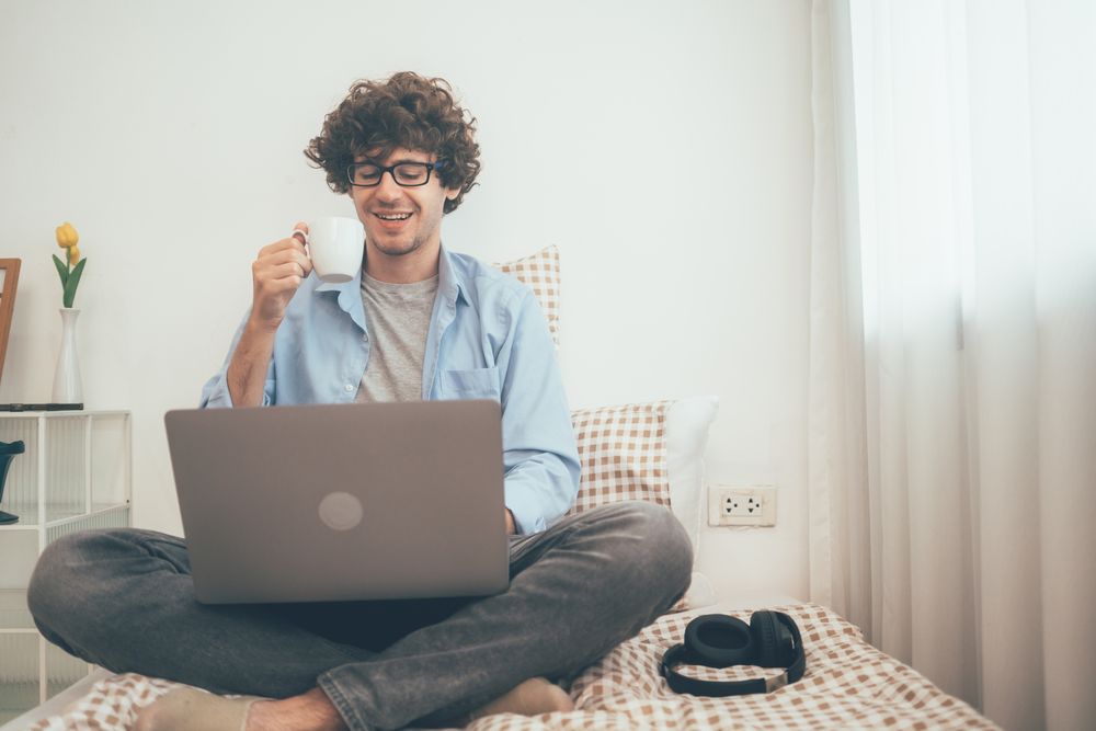 Happy man drinking coffee and working on laptop at home