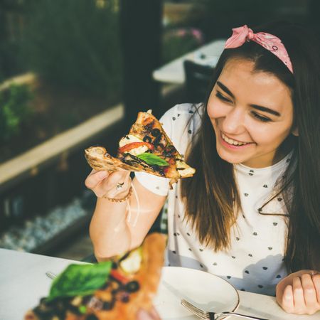 Young woman eating pizza outside, square crop