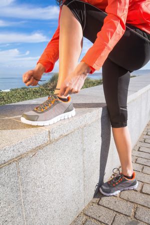 Fit woman tying shoes before work out on the beach, vertical