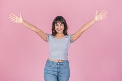 Cheerful woman with open arms wearing a breast cancer pink ribbon over pink background.  Victory to breast cancer concept.