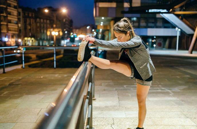 Woman runner stretching her leg before training at night in town