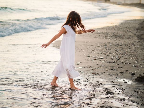 Adorable girl walking and playing on seaside at sunset