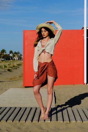 A long hair fashion model with a hat at the beach in front of a red wall