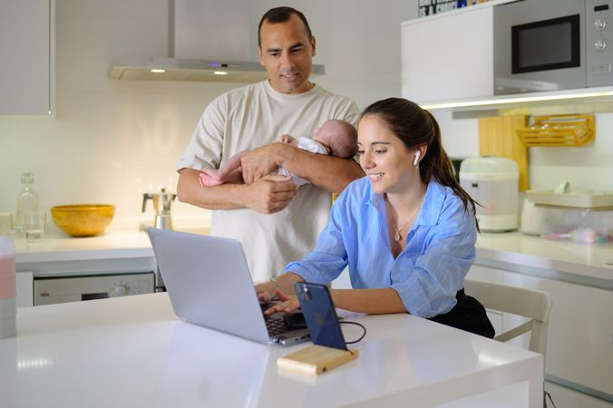 A man and woman holding a baby in front of a laptop
