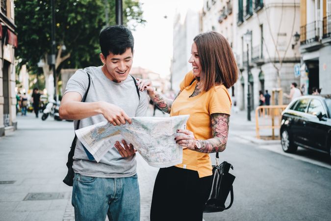 Joyful multiracial tourists checking map and standing on urban street
