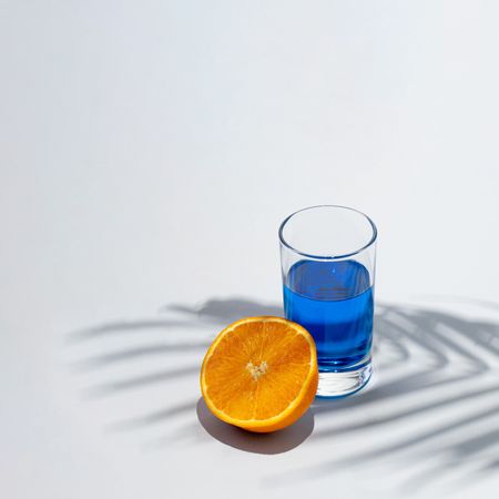 Cold blue drink glass with orange half under green palm branch