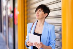 Woman in blue blazer on street standing with digital tablet