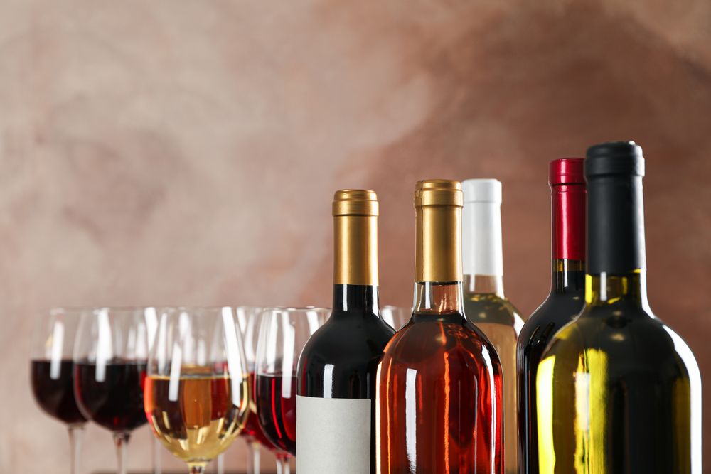 Bottles and glasses with wine against brown background, copy space