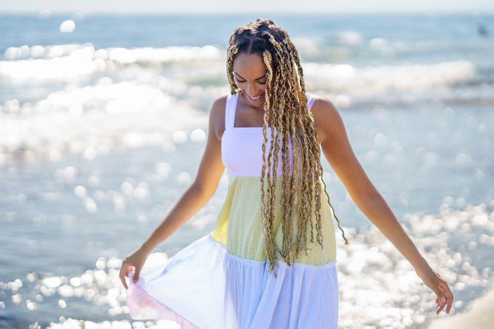 Black female looking down while walking along the shore in colorful dress