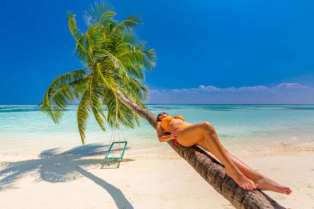 Woman leaning palm tree on a tropical beach