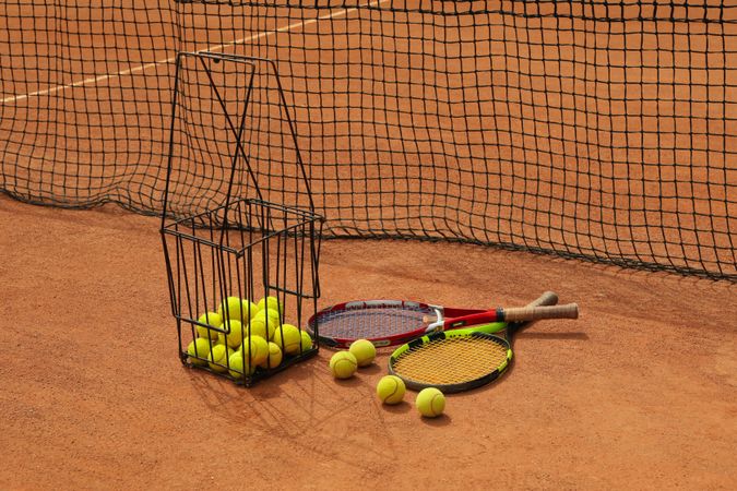 Rackets and basket with tennis balls on clay court