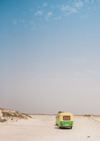 Colorful minibus with trailer parked on sandy shore in sunny day