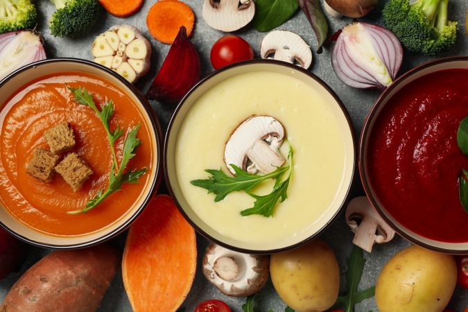 Close up of three multi-colored soups surrounded with vegetables, top view