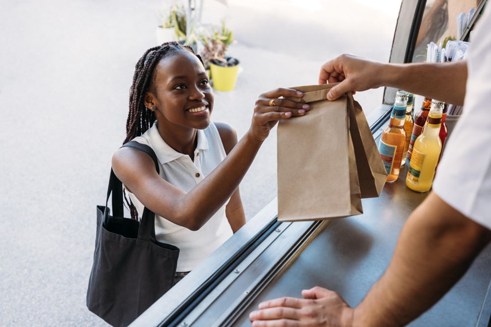 Smiling woman picking up food in paper bag from vendor