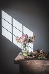 Bunch of flowers in vase near dry leaves on table