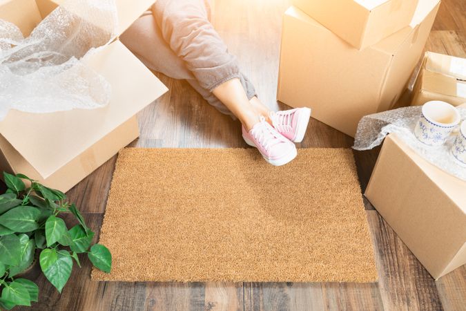 Woman Wearing Sweats Relaxing Near Home Sweet Home Welcome Mat, Moving Boxes and Plant