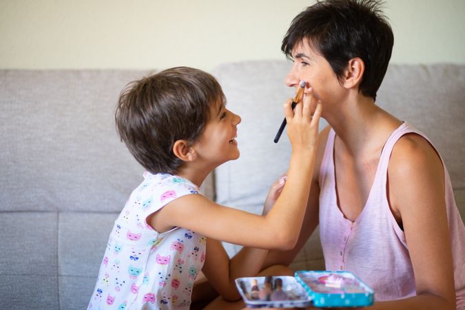 Little girl playing with make up brushes on her mother’s face