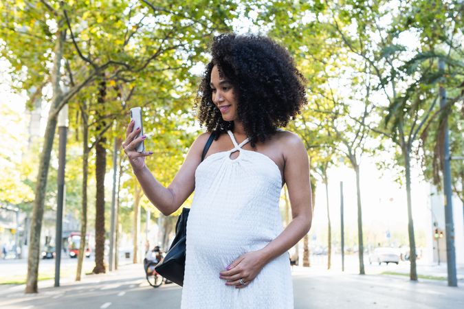 Smiling Black pregnant woman taking selfie on smartphone