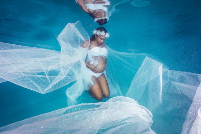 Pregnant woman in wreath and dress underwater
