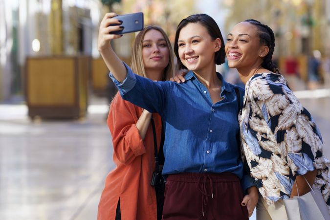 Three happy women taking selfie with phone in city, copy space