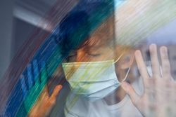 Boy in mask with hands on window at home