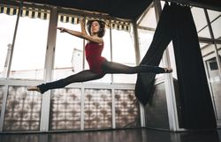 Young slim ballerina jumping above ground in studio flexing legs.