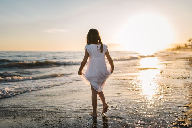 Adorable girl walking on seaside at sunset