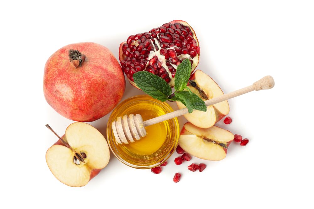 Looking down at pot of honey with dipper, split pomegranate and apples